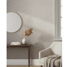 Lichte kamer met structuurbehang in visgraatpatroon, een ronde spiegel, houten tafel en een comfortabele fauteuil.