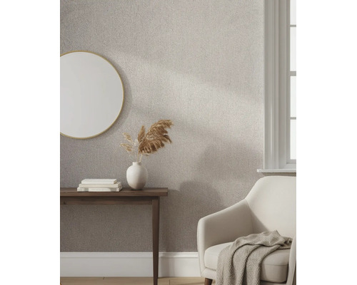 Lichte kamer met structuurbehang in visgraatpatroon, een ronde spiegel, houten tafel en een comfortabele fauteuil.