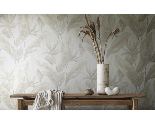 Behang met groot bladmotief in lichte tinten achter een houten bank met decoratie.
