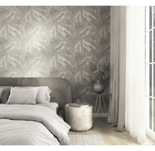 Slaapkamer met vliesbehang met botanisch bladerpatroon, bed met textiel en moderne bijzettafel bij een licht raam.