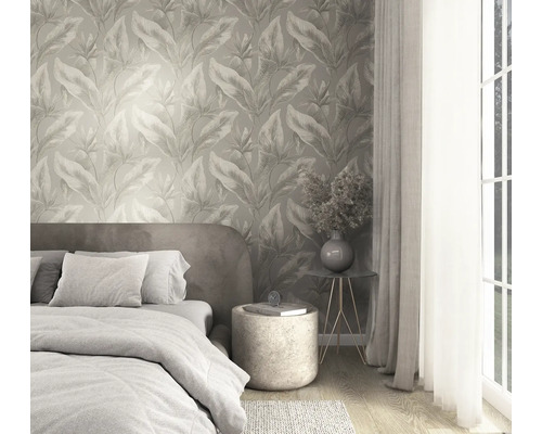 Slaapkamer met vliesbehang met botanisch bladerpatroon, bed met textiel en moderne bijzettafel bij een licht raam.