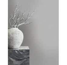 Minimalistisch interieur met een grijze muur, een gestructureerde vaas op een marmeren sokkel en decoratieve takken.