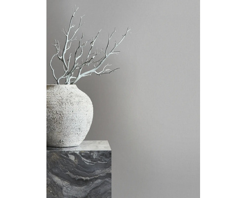 Minimalistisch interieur met een grijze muur, een gestructureerde vaas op een marmeren sokkel en decoratieve takken.