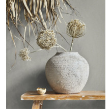 Rustieke keramische vaas met textuur en droogbloemen op een houten bankje voor een wand.