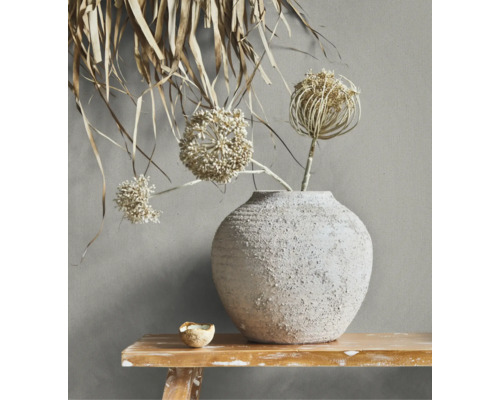 Rustieke keramische vaas met textuur en droogbloemen op een houten bankje voor een wand.