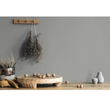 Grijze wand met structuur, gedecoreerd met een houten wandhaak, gedroogde kruiden, een houten schaal met walnoten en decoratief fruit.