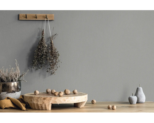 Grijze wand met structuur, gedecoreerd met een houten wandhaak, gedroogde kruiden, een houten schaal met walnoten en decoratief fruit.