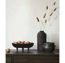 Zwarte decoratieve schaal op pootjes gevuld met walnoten naast een donkere vaas met droogbloemen op een houten dressoir.