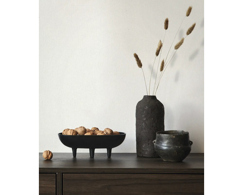 Zwarte decoratieve schaal op pootjes gevuld met walnoten naast een donkere vaas met droogbloemen op een houten dressoir.
