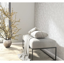 Licht interieur met een gestoffeerde zitbank, gestreepte kussens, een plaid, geometrisch behang en een decoratieve kunstplant.