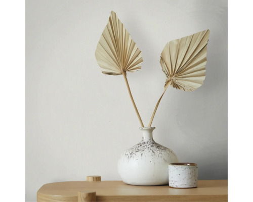 Twee gedroogde waaiervormige palmbladeren in een gespikkelde keramische vaas op een lichte houten tafel, minimalistische en lichte decoratie.