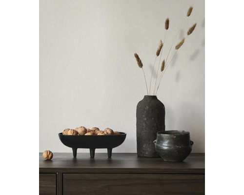 Dressoir van donker hout met een decoratieve zwarte schaal op drie poten gevuld met walnoten, een vaas met droogbloemen en een pot.