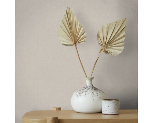 Minimalistische decoratie met een gespikkelde keramieken vaas, twee gedroogde palmbladeren en een bijpassend potje op een houten oppervlak.