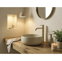 Lichte badkamer met een ronde opzetwastafel op een houten blad, een hoge goudkleurige kraan en een ronde wandspiegel.