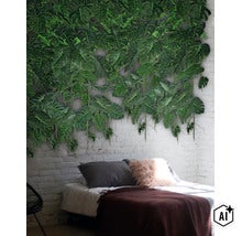Kunstmatige Monstera bladeren wanddecoratie op een witte bakstenen muur boven een bed in een modern ingerichte slaapkamer. (Image AI modified or generated)