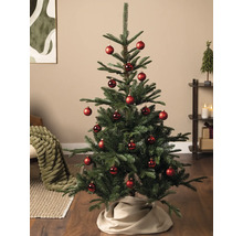 Kunstkerstboom gedecoreerd met rode kerstballen in een lichte woonkamer op een houten vloer.