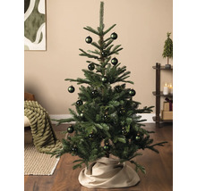 Kleine groene kerstboom versierd met donkergroene kerstballen in een lichte, modern ingerichte woonkamer.