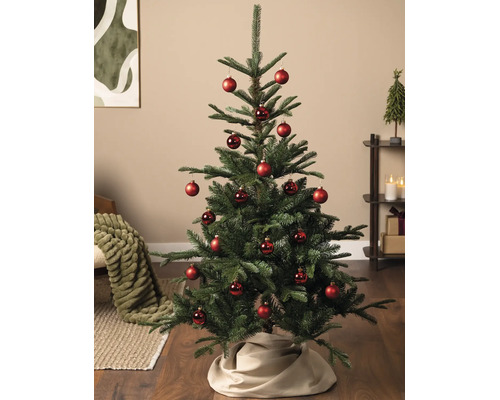 Kunstkerstboom gedecoreerd met rode kerstballen in een lichte woonkamer op een houten vloer.