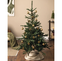 Kunstkerstboom gedecoreerd met gouden kerstballen en een beige kerstboomrok in een woonkamer.