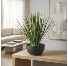 Kunstplant in ronde pot op een houten tafel in een lichte, moderne woonkamer met bank en marmeren tafel.