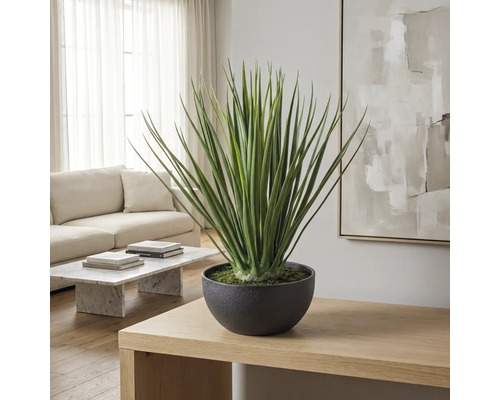 Kunstplant in ronde pot op een houten tafel in een lichte, moderne woonkamer met bank en marmeren tafel.