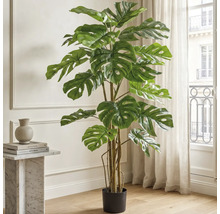 Kunstmatige Monstera Deliciosa plant in een zwarte pot, staand in een lichte woonkamer naast een marmeren tafel.