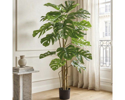 Kunstmatige Monstera Deliciosa plant in een zwarte pot, staand in een lichte woonkamer naast een marmeren tafel.
