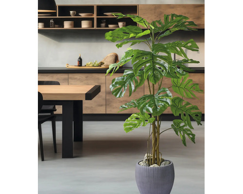 Kunstmatige Monstera plant in een antracietkleurige pot, staand in een moderne keuken met houten elementen en een grijze vloer.