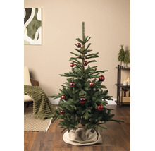 Groene kerstboom versierd met rode kerstballen in een sfeervolle woonkamer met fauteuil, rek en kerstdecoratie.