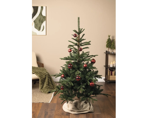 Groene kerstboom versierd met rode kerstballen in een sfeervolle woonkamer met fauteuil, rek en kerstdecoratie.