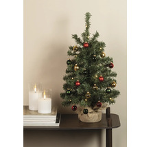 Gedecoreerde kunstkerstboom met LED-verlichting en juten voet naast witte kaarsen op een tafel.
