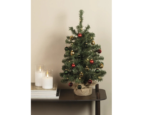 Gedecoreerde kunstkerstboom met LED-verlichting en juten voet naast witte kaarsen op een tafel.