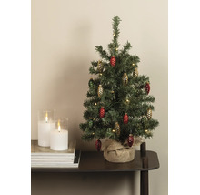 Kleine kunstkerstboom met dennenappelornamenten en warmwitte verlichting, voet omwikkeld met jute, op een tafel naast kaarsen.