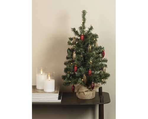 Kleine kunstkerstboom met dennenappelornamenten en warmwitte verlichting, voet omwikkeld met jute, op een tafel naast kaarsen.