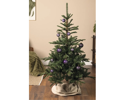 Een kerstboom versierd met paarse kerstballen met een wit sneeuwvlokpatroon, staand op een houten vloer.
