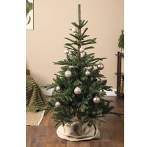 Gedecoreerde kerstboom met glanzende kerstballen en een boomrok in een lichte, sfeervolle woonkamer.