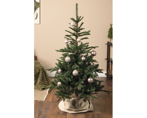 Gedecoreerde kerstboom met glanzende kerstballen en een boomrok in een lichte, sfeervolle woonkamer.