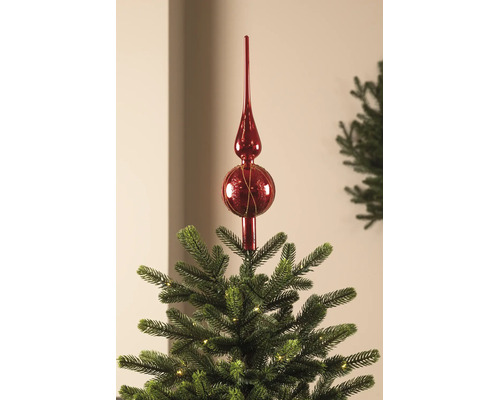 Rode glazen kerstboompiek op de top van een verlichte kerstboom.