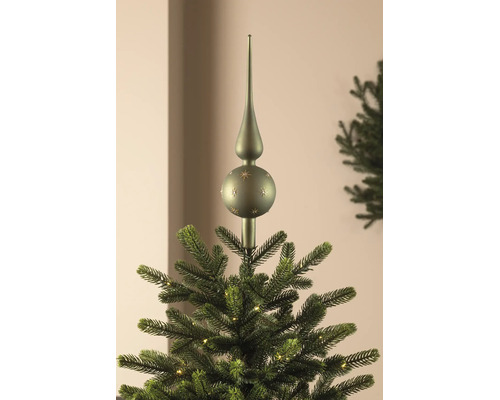 Groene glazen kerstboompiek met sterrendecor, geplaatst op de top van een verlichte kerstboom.