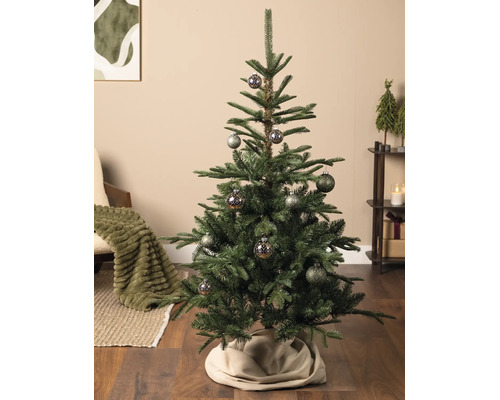 Kunstkerstboom met gedecoreerde kerstballen in een sfeervolle woonkamer met houten vloer en kerstversiering.