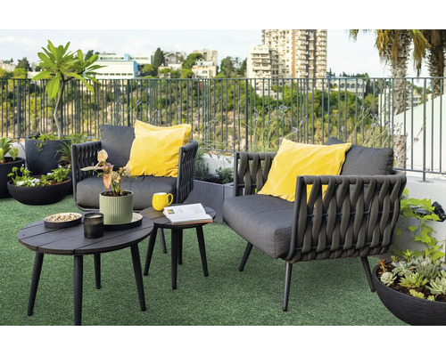 Moderne loungeset voor buiten op een dakterras met twee grijze fauteuils, gele kussens, bijzettafels en diverse plantenbakken op kunstgras.