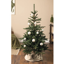 Helder gedecoreerde kunstkerstboom in een woonkamer, versierd met witte kerstballen met ruitpatroon en een beige boomrok.