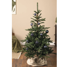 Groene kerstboom versierd met blauwe kerstballen met patronen op een houten vloer met een beige kerstboomrok.