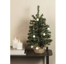 Kleine kunstkerstboom met LED-verlichting en ballen, voet omwikkeld met jute, op een tafel naast kaarsen.