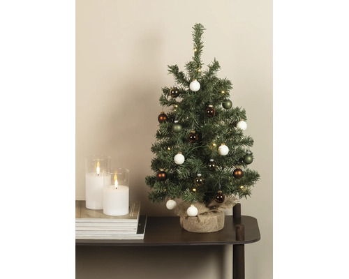 Kleine kunstkerstboom met LED-verlichting en ballen, voet omwikkeld met jute, op een tafel naast kaarsen.