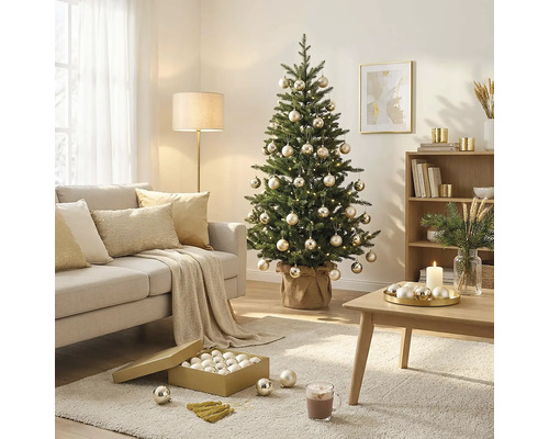 Gedecoreerde kerstboom met kerstballen en lampjes in een lichte woonkamer met bank, salontafel en vloerkleed.