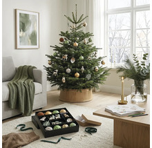 Feestelijk versierde kerstboom in een lichte woonkamer met bank, houten tafel en kerstversiering.