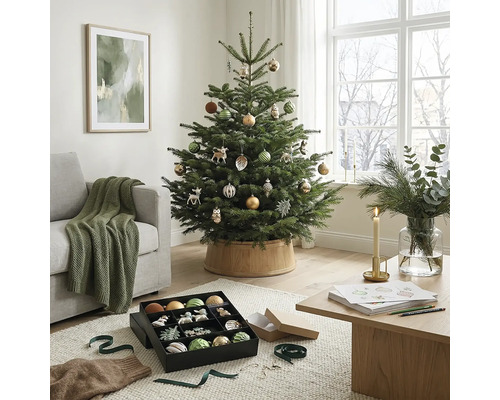 Feestelijk versierde kerstboom in een lichte woonkamer met bank, houten tafel en kerstversiering.