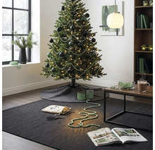 Feestelijk versierde kerstboom met donkere kerstballen en parelslingers in een modern ingerichte woonkamer met tapijt en bijzettafel.