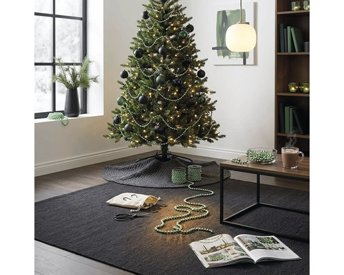 Feestelijk versierde kerstboom met donkere kerstballen en parelslingers in een modern ingerichte woonkamer met tapijt en bijzettafel.